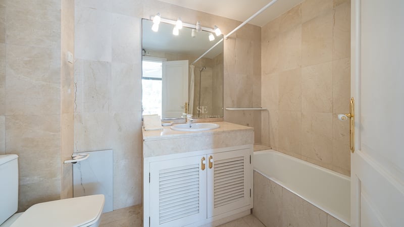 Salle de bains de style méditerranéen avec carrelage en marbre crème, baignoire intégrée et meuble vasque blanc.
