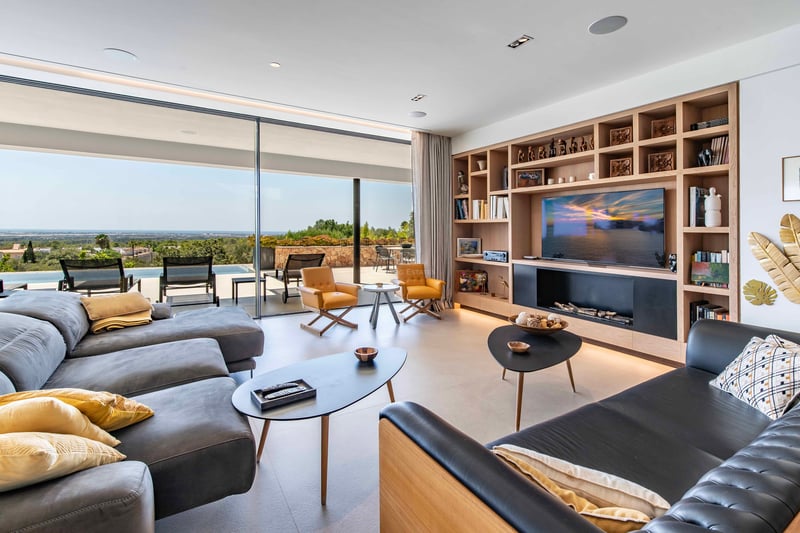Salon contemporain avec baies vitrées ouvrant sur une terrasse, piscine à débordement et vue sur le littoral.