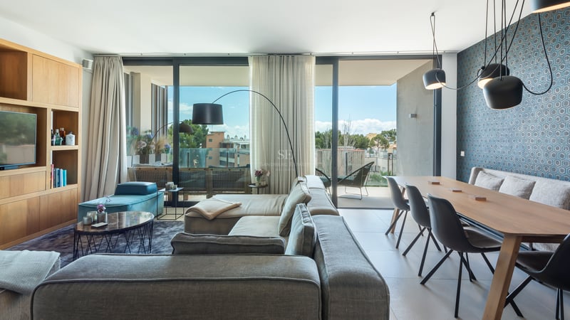 Espace de vie moderne avec canapé gris, salle à manger en bois et grandes baies vitrées menant à une terrasse.