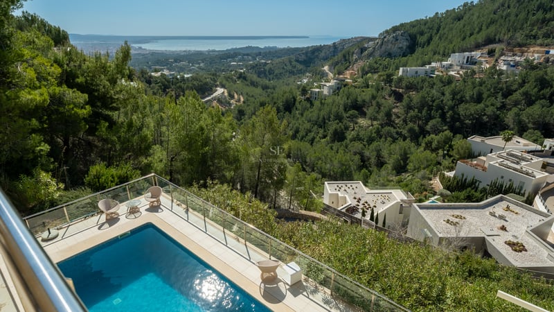 Vue surélevée d'une piscine turquoise sur une terrasse en pierre dominant une vallée verdoyante et la mer.