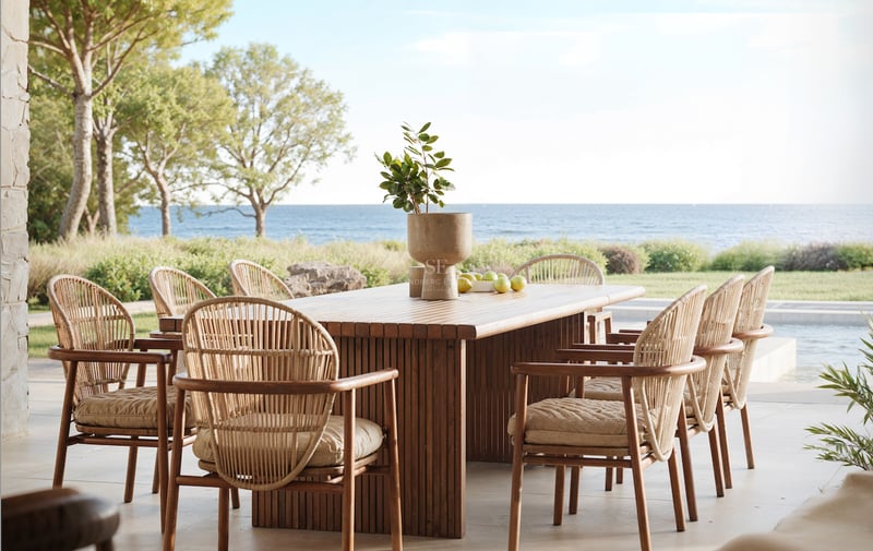 Une table à manger en bois et six chaises en osier sur une terrasse en pierre surplombant la mer Méditerranée.