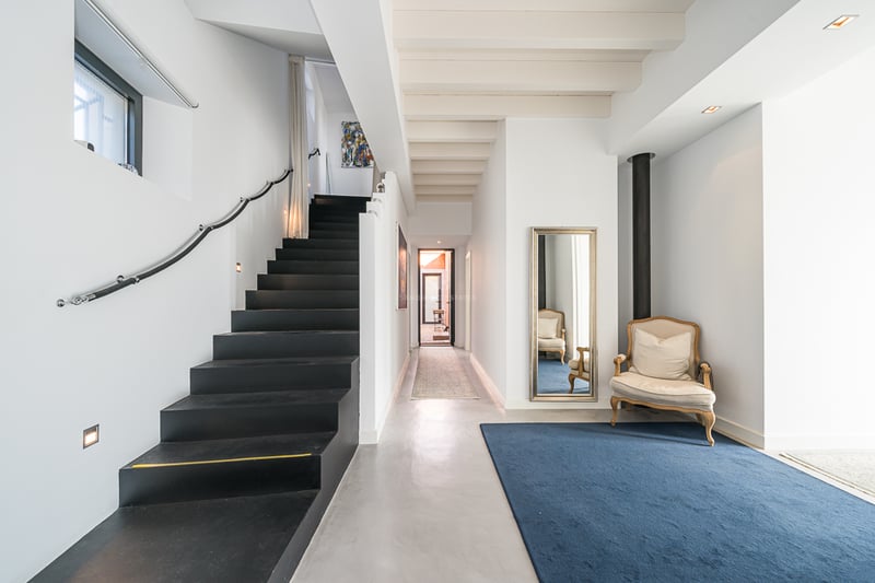 Entrée moderne comprenant un escalier noir élégant, des sols en béton poli et un tapis bleu avec un fauteuil classique.
