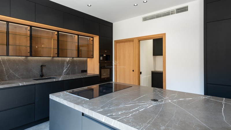 Cuisine moderne avec des armoires noir mat, des plans de travail en marbre gris et des accents en bois.
