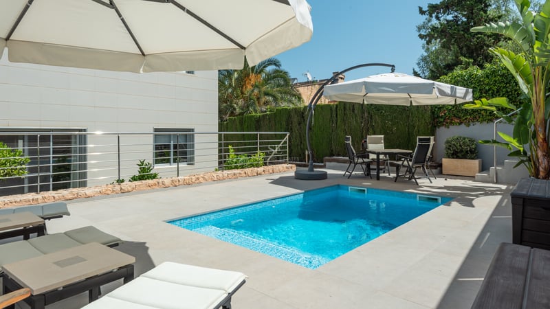 Piscine rectangulaire moderne avec terrasse en pierre, bains de soleil et coin repas sous parasols.