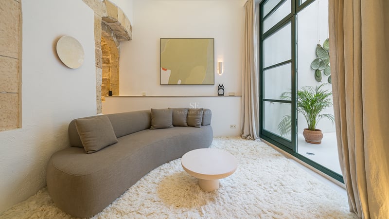 Salon moderne avec canapé gris courbé, tapis blanc épais, arche en pierre et grandes portes vitrées.