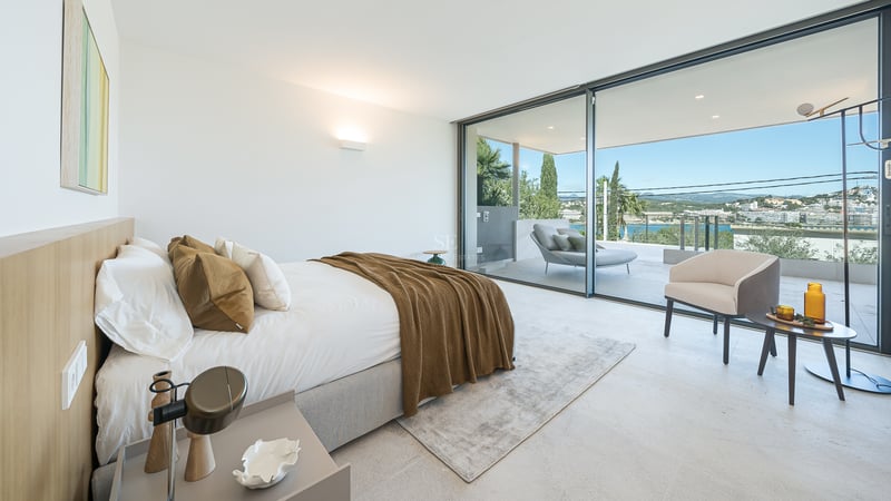Chambre moderne avec de grandes baies vitrées s'ouvrant sur une terrasse surplombant une ville côtière et la mer.