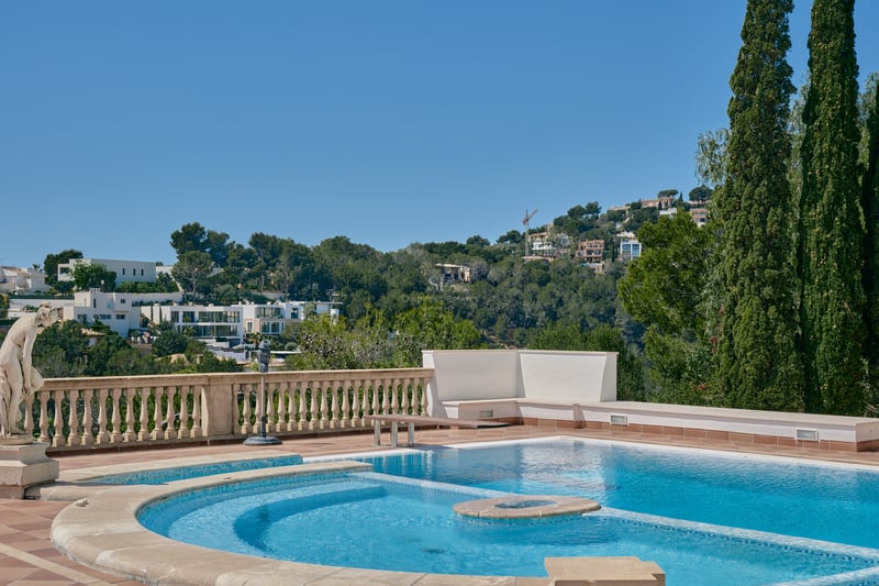 Piscine ensoleillée avec balustrade en pierre et statue classique surplombant une vallée verdoyante et des villas.