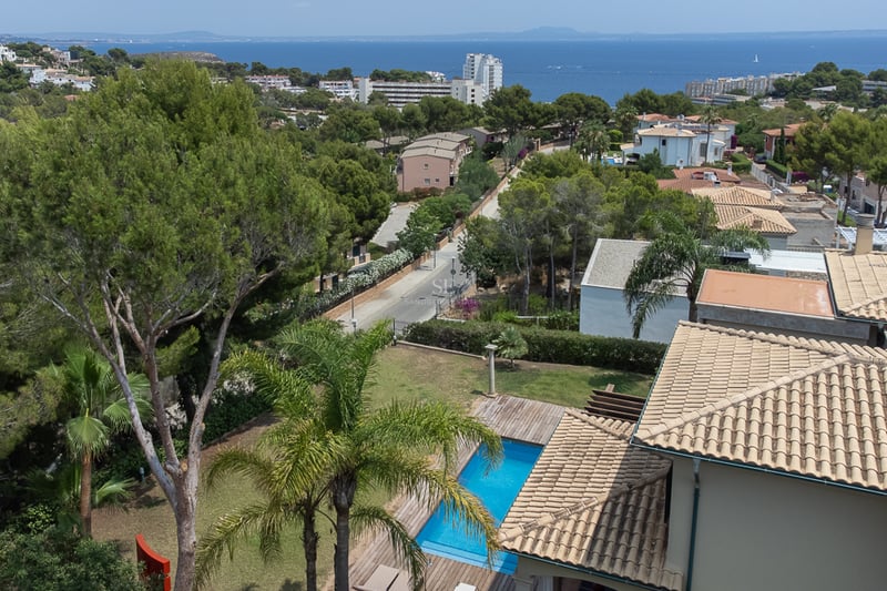 Vue surélevée d'une piscine et de toits en terre cuite avec la mer Méditerranée et la côte à l'horizon.