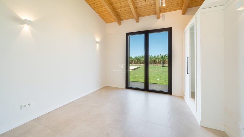 Dormitorio con techo de vigas de madera, puertas de cristal al jardín y armarios empotrados blancos.