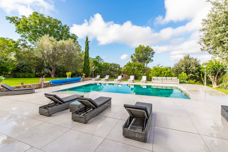 Grande piscine aux eaux turquoises entourée d'une terrasse en carrelage beige avec bains de soleil et jardin luxuriant.
