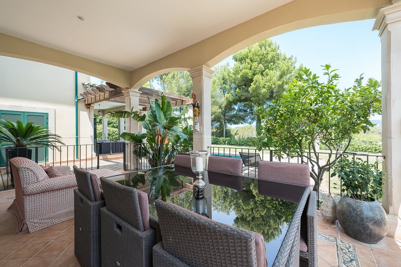 Une terrasse couverte avec un ensemble de salle à manger en rotin, sol en terre cuite et colonnes cintrées.
