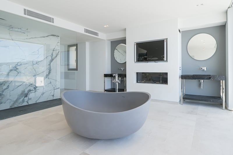 Salle de bain moderne avec baignoire grise, douche en marbre et doubles vasques avec miroirs ronds.