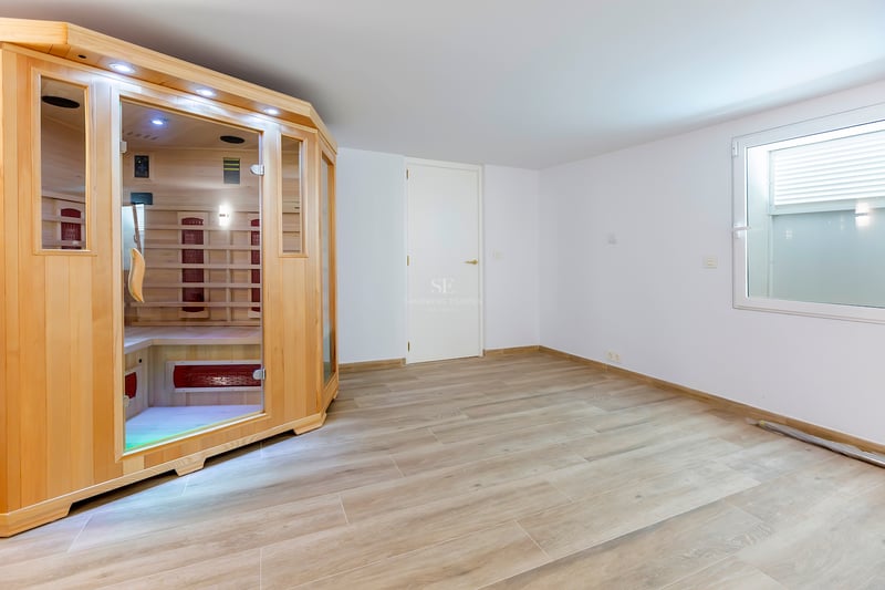 Pièce moderne avec cabine de sauna en bois clair, portes vitrées et sol en grès cérame imitation bois.