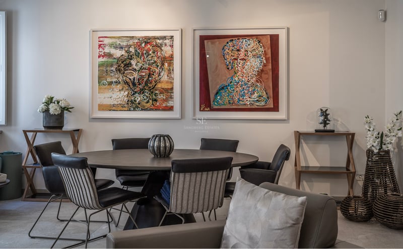 Salle à manger moderne avec table ronde sombre, chaises design et deux grands tableaux abstraits au mur blanc.