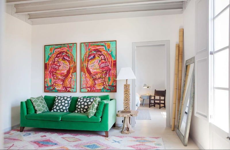 Sala de estar luminosa con sofá de terciopelo verde, dos grandes cuadros coloridos y techos altos con vigas.