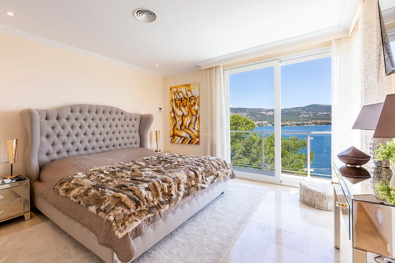 Chambre élégante avec grand lit, tête de lit capitonnée, sol en marbre et baies vitrées offrant une vue sur la mer.