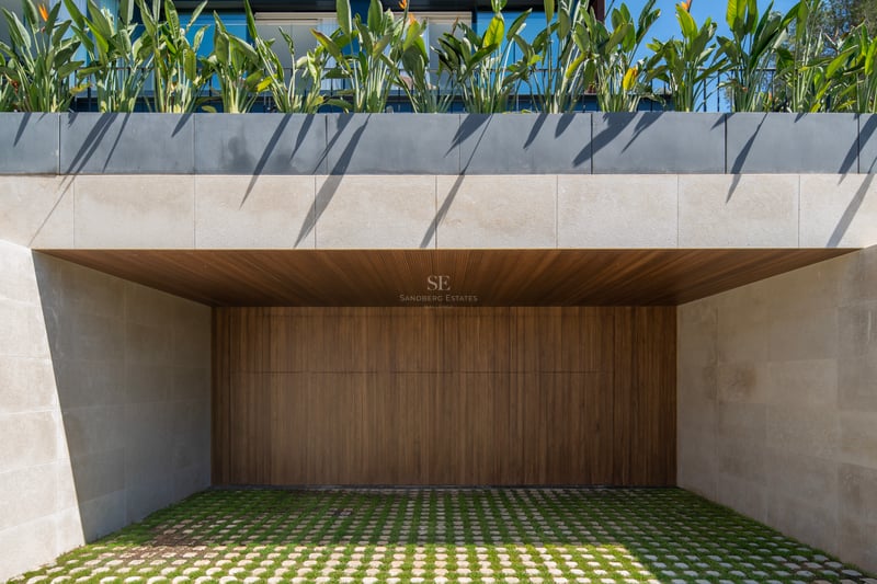 Entrée de garage contemporaine avec porte en bois à lattes, murs en pierre naturelle et pavés drainants végétalisés.