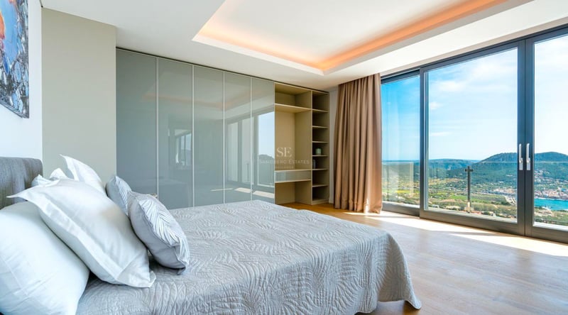 Chambre moderne avec baies vitrées donnant sur la côte, placards intégrés et parquet en bois.