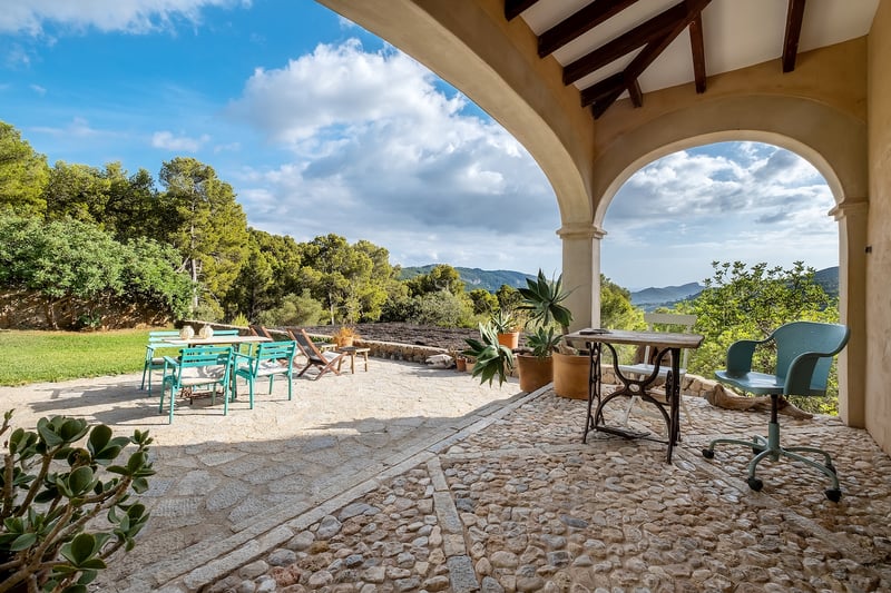 Terrasse en pierre avec arches donnant sur une vallée verdoyante et des montagnes, avec mobilier d'extérieur bleu sarcelle et bois.