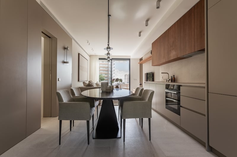 Salle à manger contemporaine avec table ovale noire, fauteuils gris et cuisine minimaliste épurée.