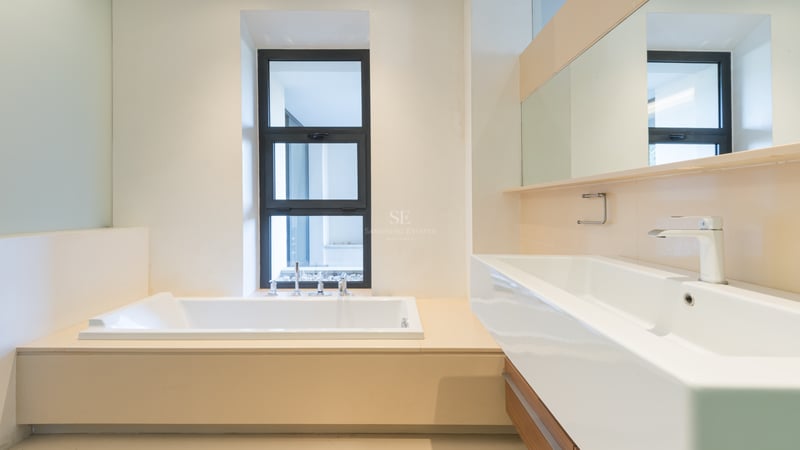 Salle de bain moderne avec une baignoire blanche encastrée près d'une fenêtre et une grande vasque rectangulaire.