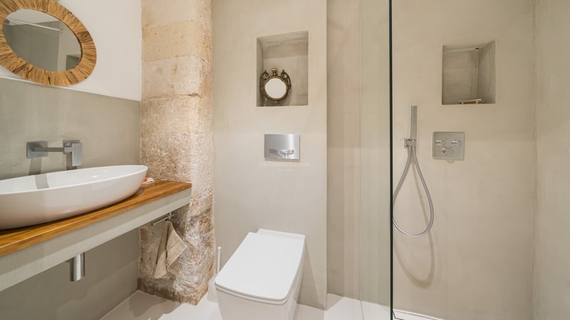 Salle de bain moderne avec vasque blanche, plan en bois, pilier en pierre et douche vitrée.