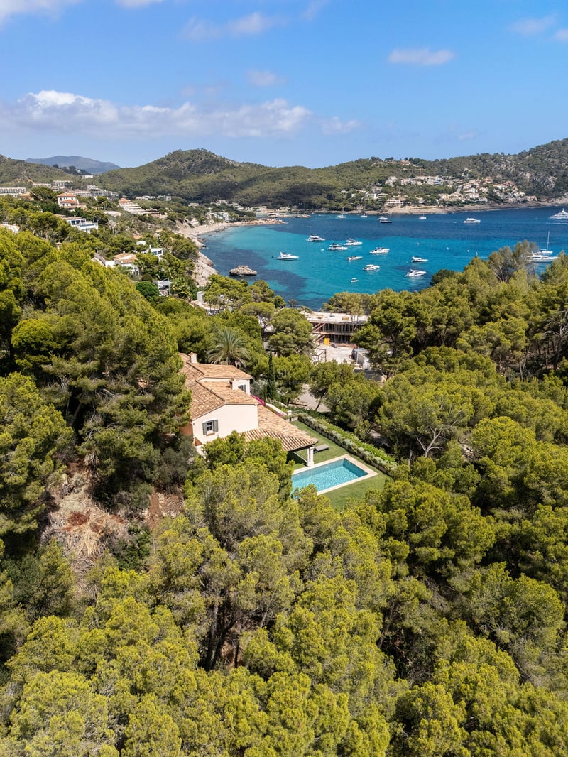 Vue aérienne d'une villa au toit de terre cuite avec piscine privée entourée d'une forêt de pins face à la mer.