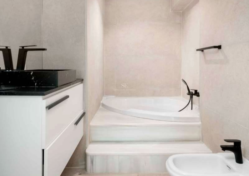 Salle de bain moderne avec baignoire intégrée, marches en marbre blanc et robinetterie noire mate.