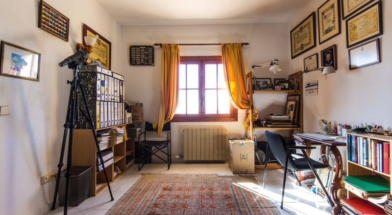 Bureau avec bureau en bois, télescope, étagères, rideaux jaunes et diplômes aux murs.