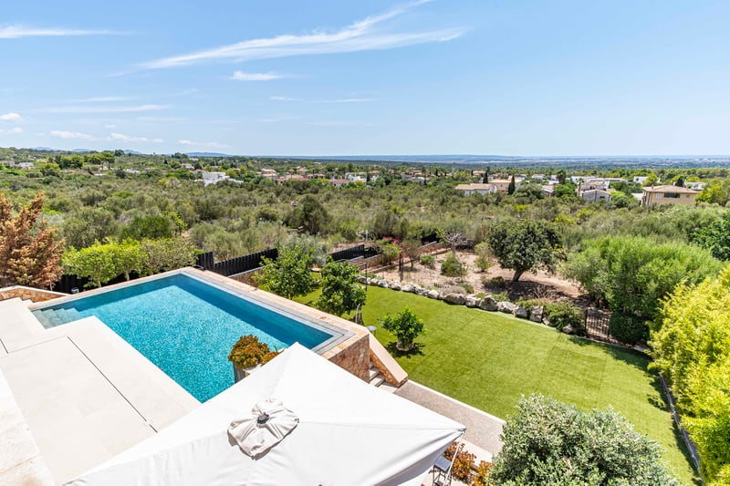 Vue aérienne d'une piscine bleue entourée d'une terrasse en pierre et d'un jardin avec vue sur l'horizon méditerranéen.