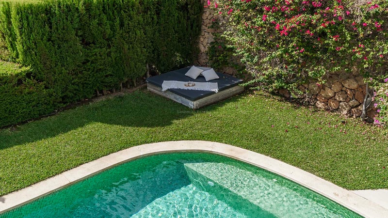 Piscine aux carreaux verts bordée d'une pelouse impeccable et d'un lit de repos sous des bougainvilliers.