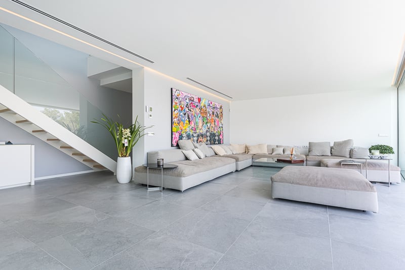 Grand salon avec canapé modulable gris, œuvre d'art murale colorée et escalier vitré.