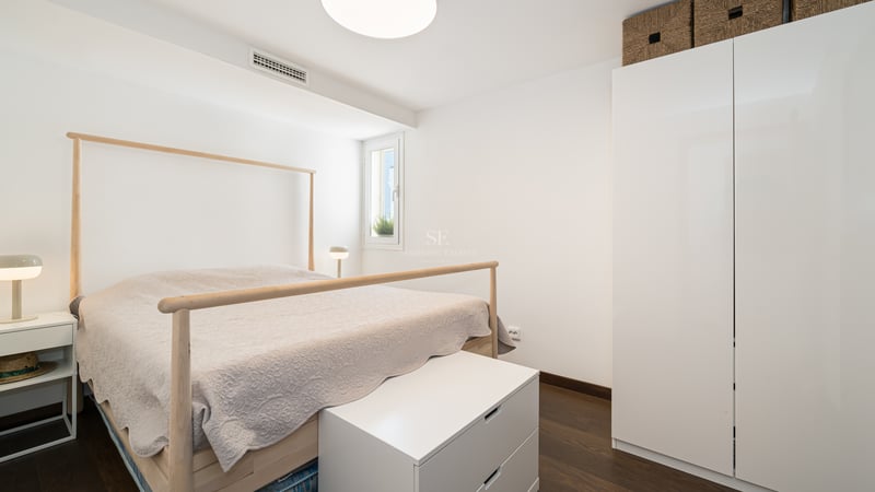 Chambre lumineuse avec cadre de lit en bois clair, armoires blanches minimalistes et parquet en bois foncé.