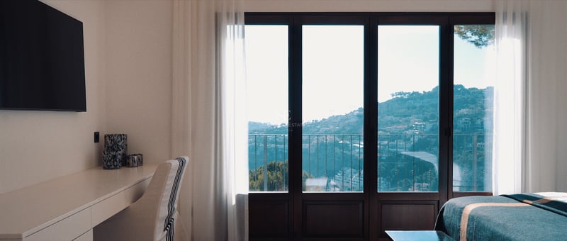 Chambre moderne avec bureau, TV murale et baies vitrées donnant sur une vue panoramique de la colline et de la mer.