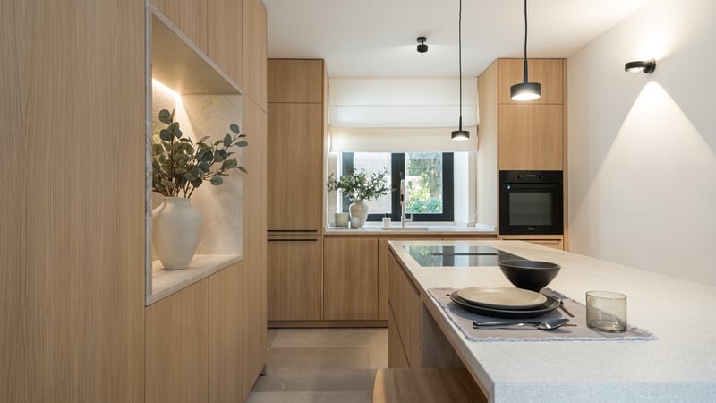 Cuisine moderne avec placards en chêne, îlot en pierre, suspensions minimalistes et niche décorative éclairée.