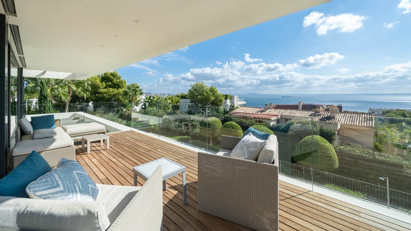 Terrasse moderne avec terrasse en bois, canapés blancs et garde-corps en verre offrant une vue sur mer.