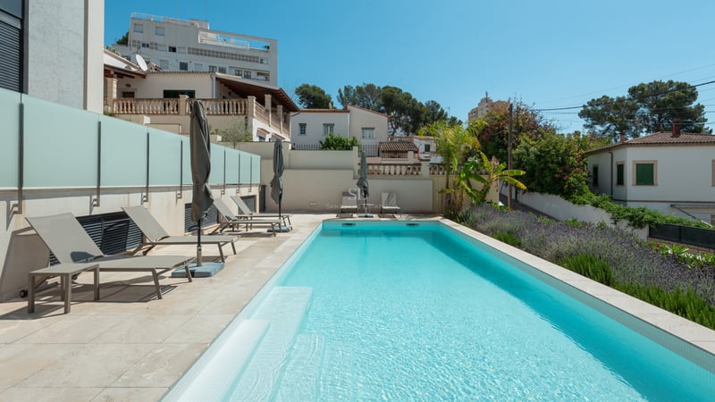 Piscine rectangulaire aux eaux turquoises, terrasse en pierre claire, bains de soleil gris et jardin méditerranéen.