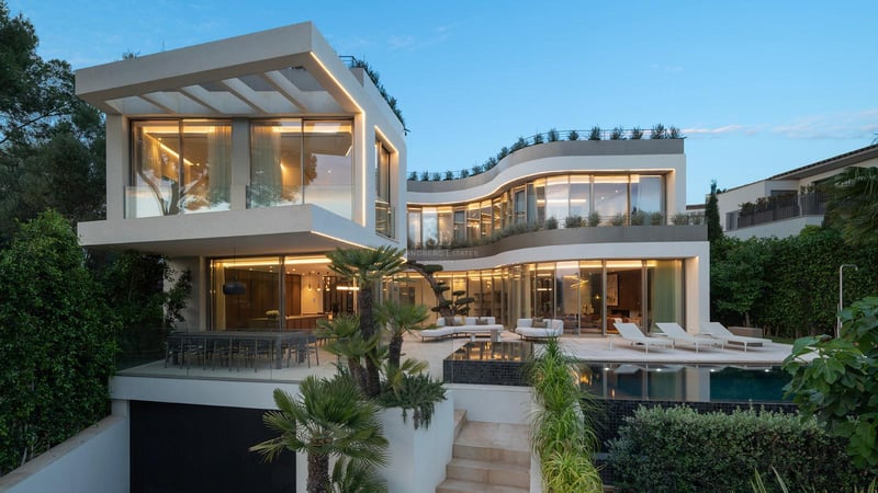 Vue nocturne d'une villa contemporaine à plusieurs niveaux avec façades vitrées courbes, terrasse et piscine éclairée.