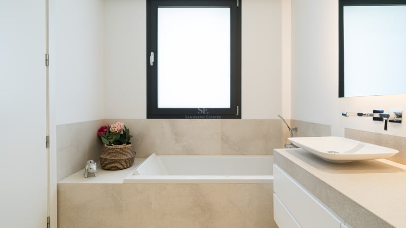 Salle de bain minimaliste avec baignoire blanche, vasque sur plan en pierre et fenêtre à cadre noir.