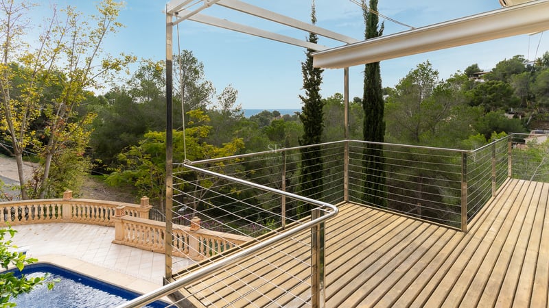 Terrasse surélevée en bois avec garde-corps métalliques surplombant une piscine et une forêt luxuriante.