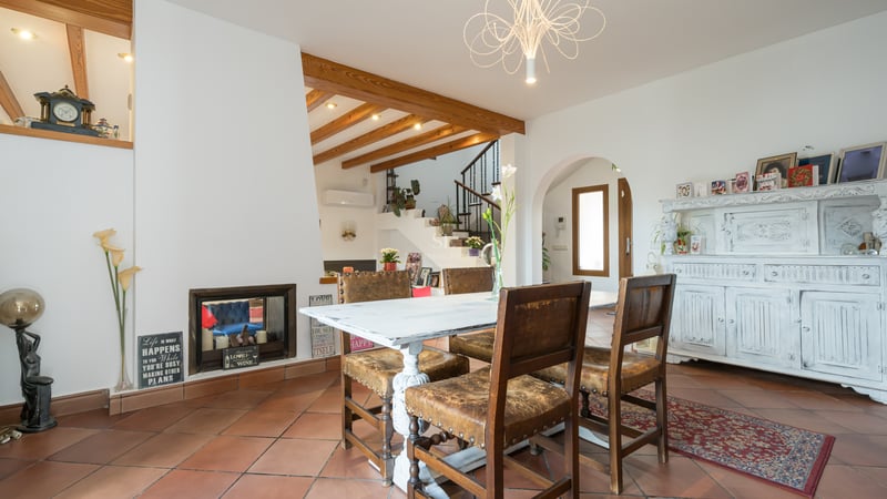 Intérieur d'une salle à manger avec sol en terre cuite, poutres en bois, table blanche vieillie et chaises en cuir.