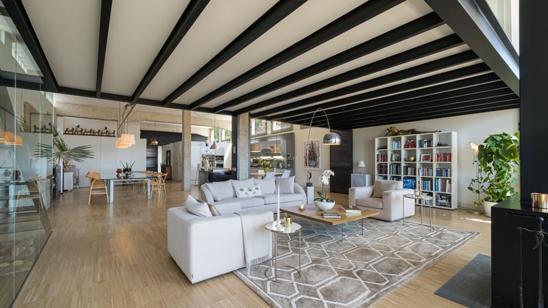 Grand salon avec poutres en acier noir, parquet clair et canapés blancs dans une villa de luxe décloisonnée.
