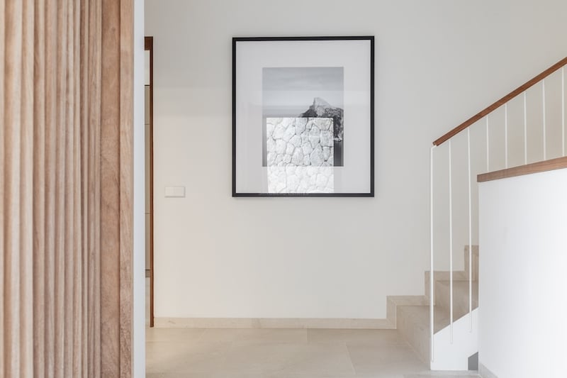 Couloir minimaliste avec escalier en pierre, main courante en bois et une grande œuvre d'art encadrée sur un mur blanc.