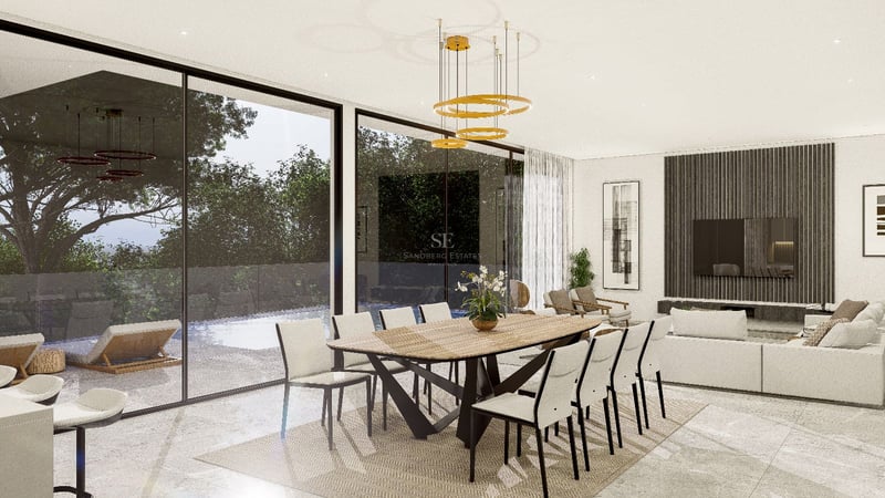 Salle à manger moderne avec table en bois, luminaire doré et baies vitrées donnant sur la piscine et le jardin.