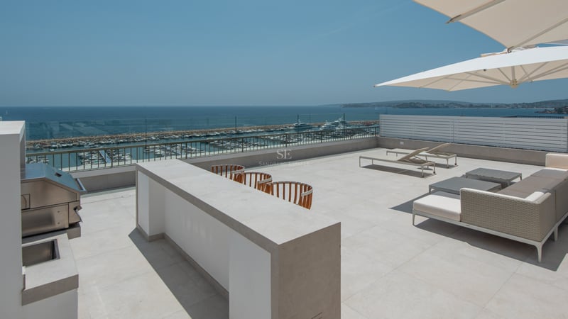 Grande terrasse sur le toit avec cuisine extérieure en inox, salon de jardin et vue sur le port de plaisance.