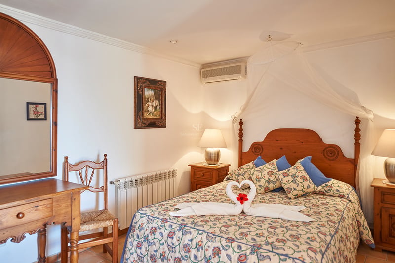 Une chambre confortable avec un lit en bois, une moustiquaire blanche, une literie fleurie et des meubles rustiques.