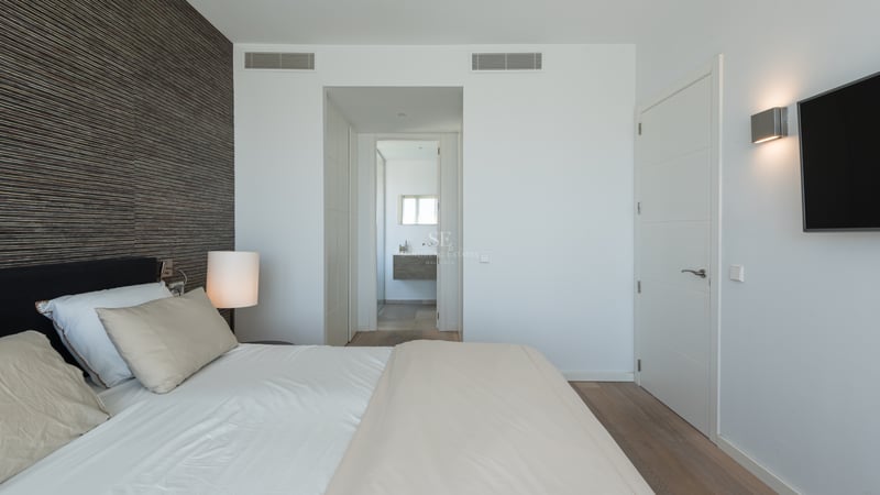Chambre parentale contemporaine avec mur d'accent en bois sombre, lit blanc et vue sur la salle de bain attenante.