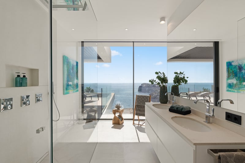 Salle de bain moderne avec douche vitrée et double vasque offrant une vue panoramique sur la mer.