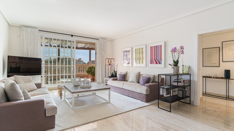 Salon lumineux avec sol en marbre, canapés mauves et grandes baies vitrées ouvrant sur une terrasse méditerranéenne.