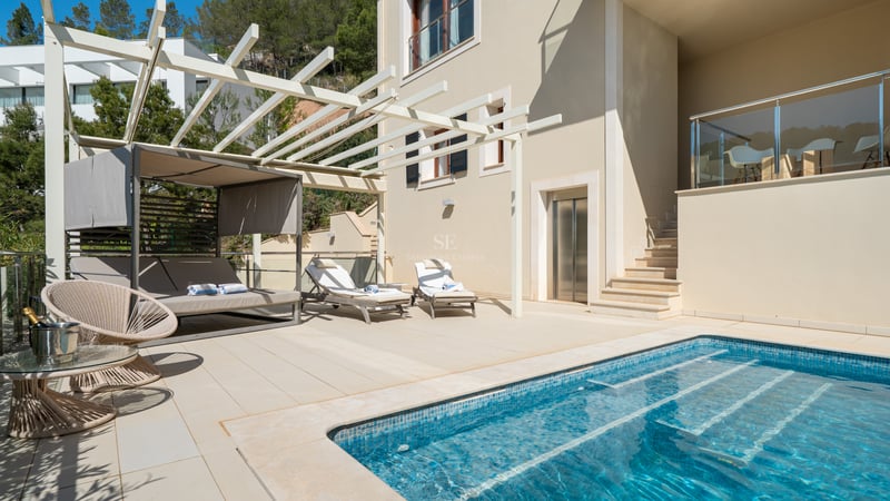 Terrasse de villa moderne avec piscine en mosaïque bleue, lits de repos et revêtement en pierre claire.